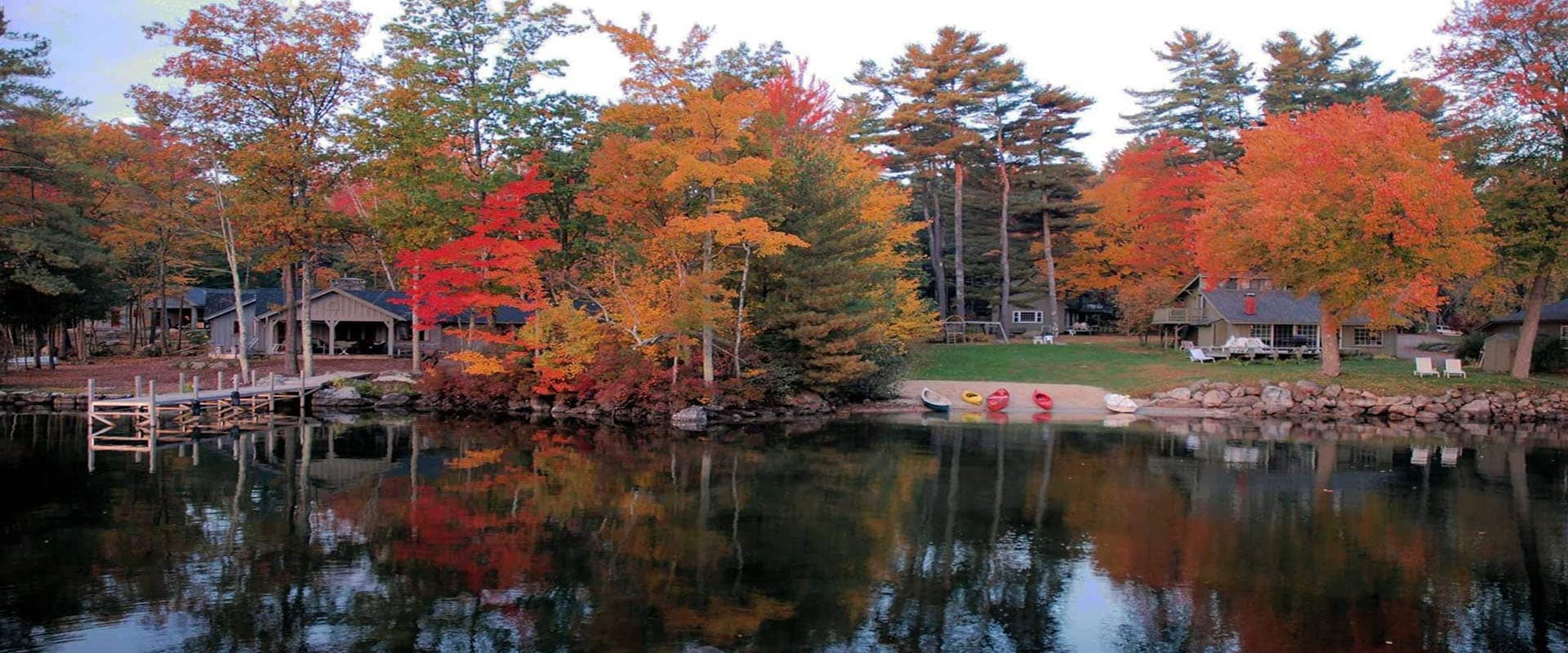 A serene lake surrounded by colorful autumn trees and wooden cabins reflecting in the water.